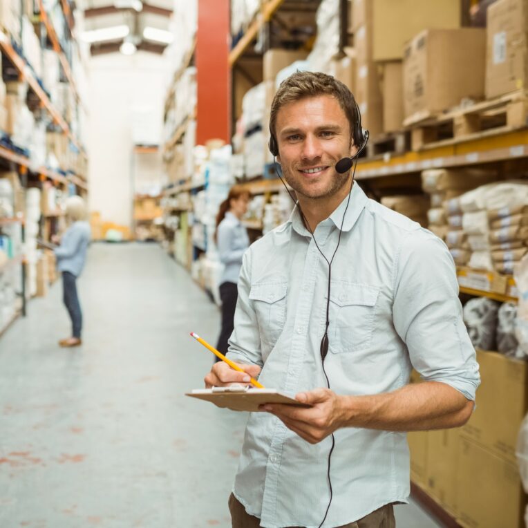 Warehouse manager wearing headset writing on clipboard