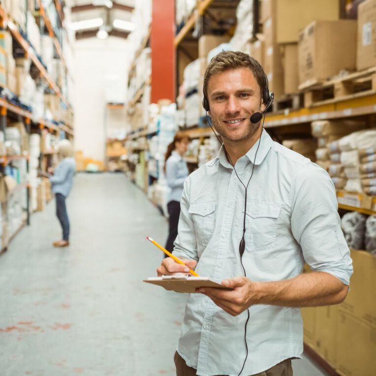 Warehouse manager wearing headset writing on clipboard
